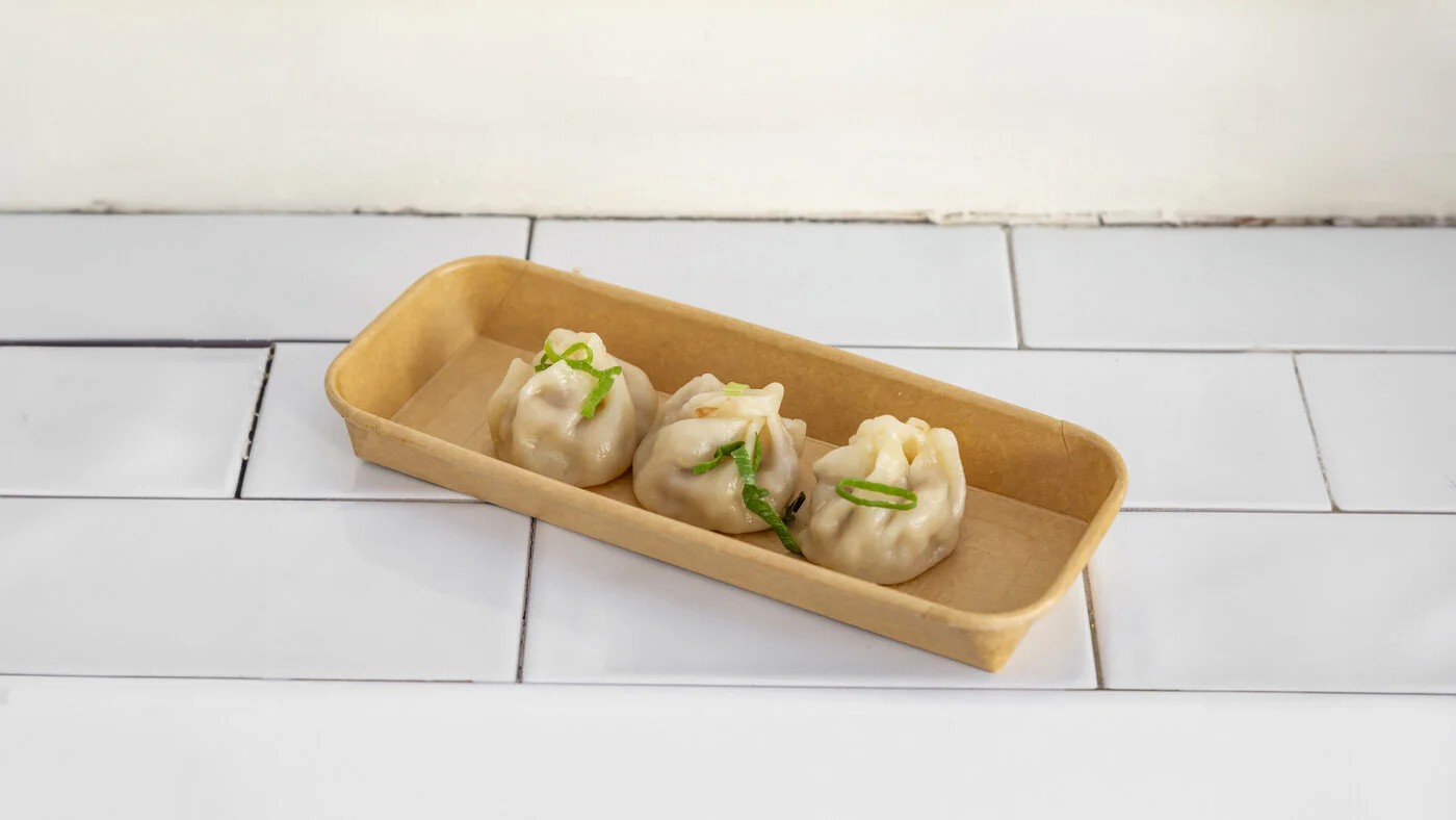 Trois xiao long bao vapeur en barquette, parsemés de ciboule