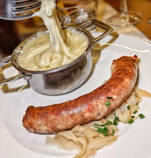 Une saucisse d'Aveyron grillée avec son aligot, tiré à la fourchette au dessus du poêlon pour montrer le fil
