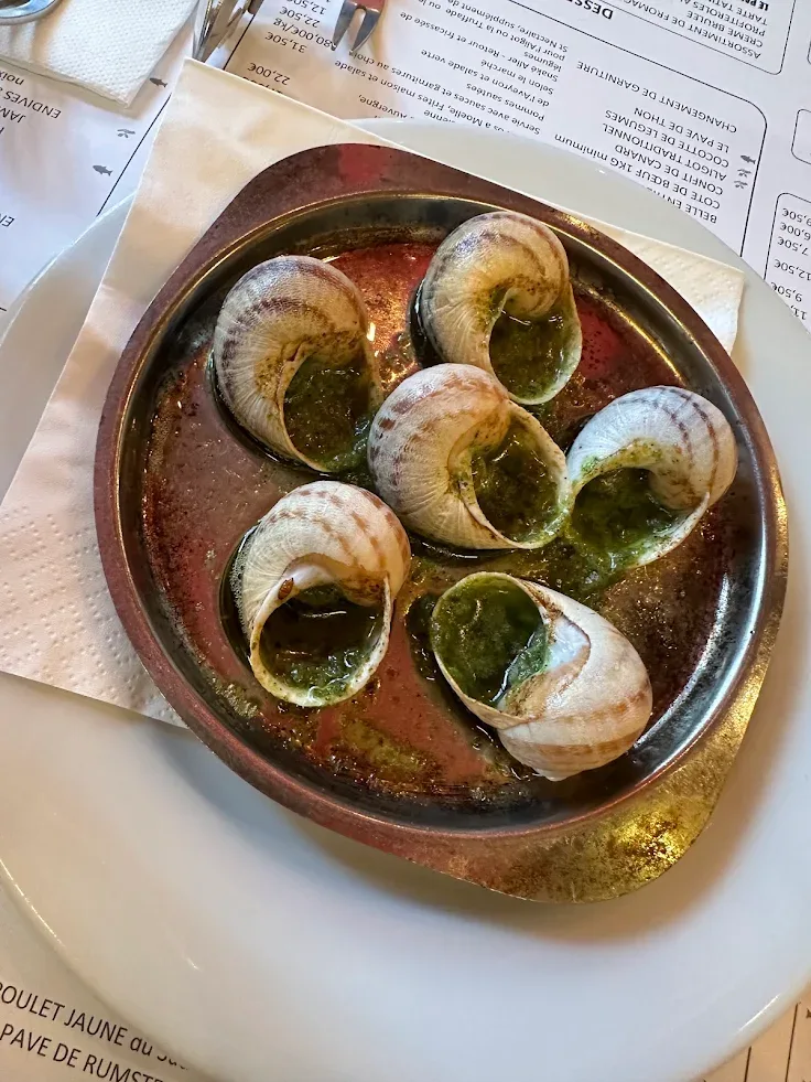 Six escargots à la bourguignonne dans leur plat en cuivre, posés sur la carte de la maison