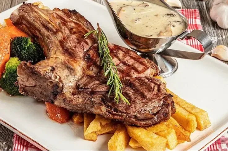 Une côte de bœuf grillée sur l'os, avec frites, légumes et une saucière de sauce aux champignons