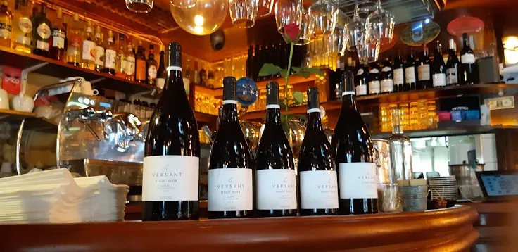 Le comptoir en bois, une rangée de magnums alignés, l'étagère à spiritueux et les verres suspendus