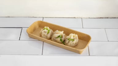 Three steamed xiao long bao in their tray, scattered with spring onion